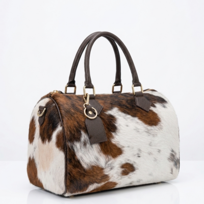 Handmade cowhide leather barrel bag in brown and white hair-on-hide, with dark leather handles and gold hardware, western style Boston satchel