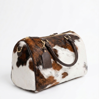 Handmade cowhide leather barrel bag in brown and white hair-on-hide, with dark leather handles and gold hardware, western style Boston satchel