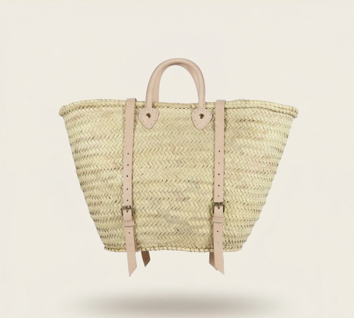 Handwoven Moroccan palm leaf straw market tote with braided leather top handles and convertible leather backpack straps with silver buckles on white surface
