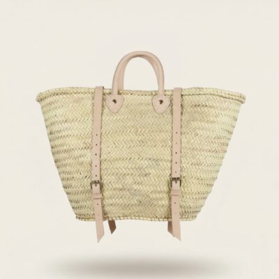 Handwoven Moroccan palm leaf straw market tote with braided leather top handles and convertible leather backpack straps with silver buckles on white surface
