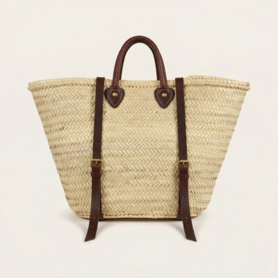 Handwoven Moroccan palm leaf straw market tote with braided leather top handles and convertible leather backpack straps with silver buckles on white surface