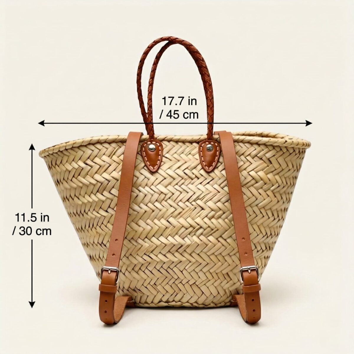 Handwoven Moroccan palm leaf straw market tote with braided leather top handles and convertible leather backpack straps with silver buckles on white surface
