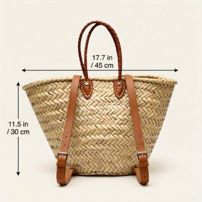 Handwoven Moroccan palm leaf straw market tote with braided leather top handles and convertible leather backpack straps with silver buckles on white surface