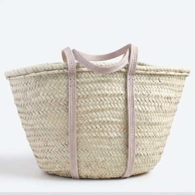Large handmade Moroccan straw market basket with embossed leather straps on rustic wooden table, surrounded by lavender and olive branches