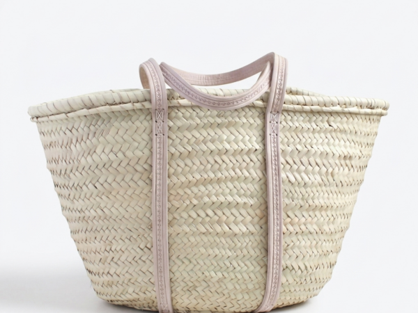 Large handmade Moroccan straw market basket with embossed leather straps on rustic wooden table, surrounded by lavender and olive branches