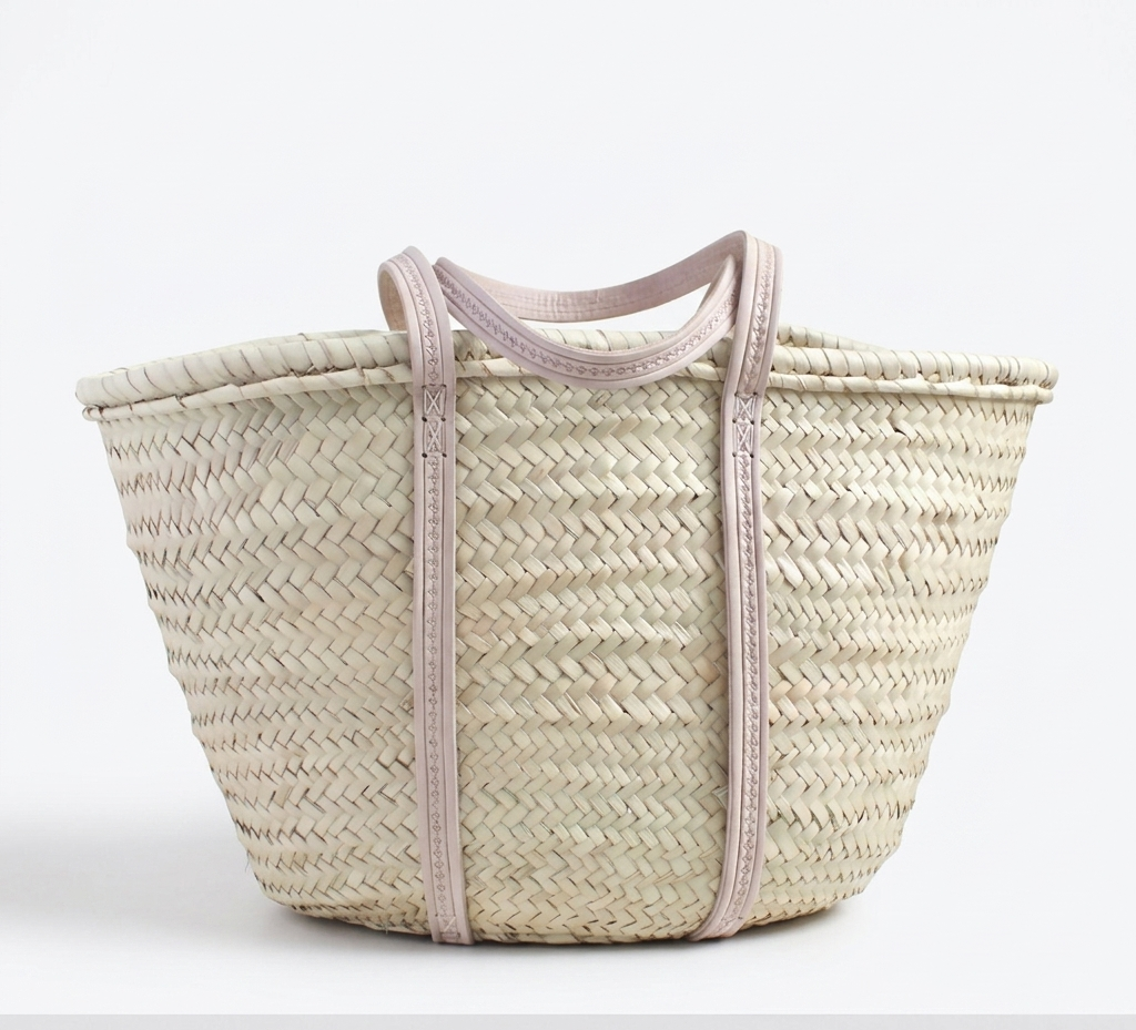 Large handmade Moroccan straw market basket with embossed leather straps on rustic wooden table, surrounded by lavender and olive branches