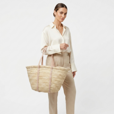 Woman carrying large handwoven Moroccan palm leaf straw French market basket tote with full-length embossed leather handles over shoulder