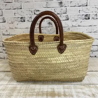 il_794xN.7593299544_6whu Handmade Moroccan palm leaf straw market basket with short dark leather loop handles and heart-shaped anchor tabs, wide oval open-top silhouette, classic French market style