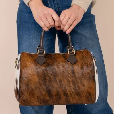 Woman holding large handmade cowhide leather bowling bag in brown and white hair-on-hide, dark leather handles, gold hardware