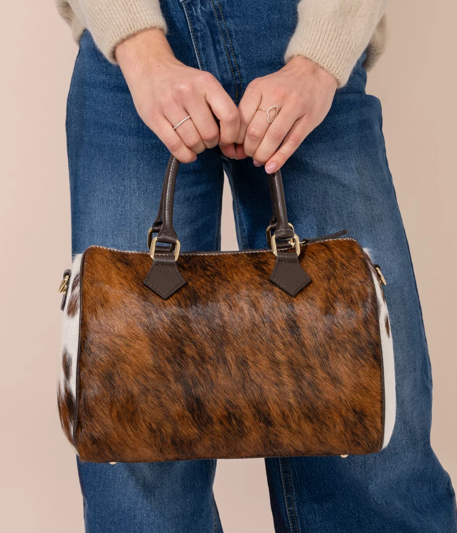 Woman holding large handmade cowhide leather bowling bag in brown and white hair-on-hide, dark leather handles, gold hardware