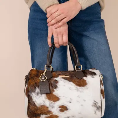 Front view of handmade cowhide Boston bowling bag in brown white natural pattern with branded gold tag and dark handles