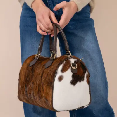 Side view of large cowhide bowling bag showing brown hair-on-hide pattern and white panel, held by model