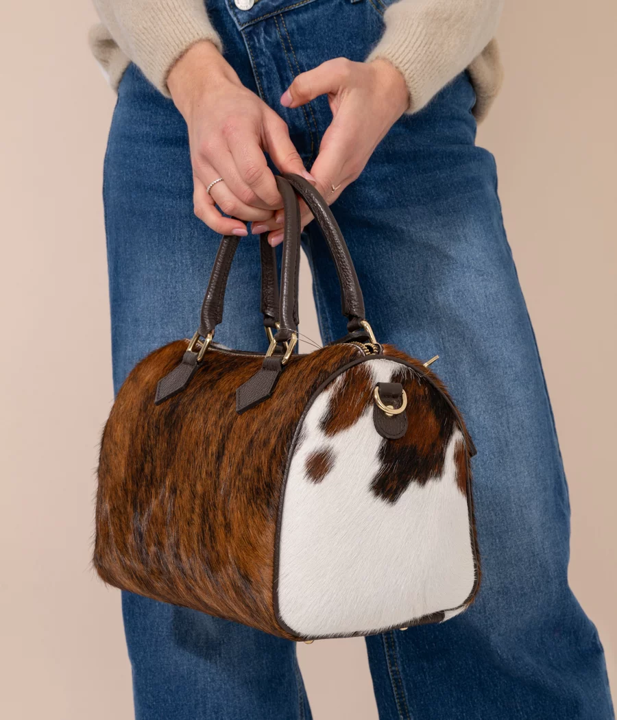 Side view of large cowhide bowling bag showing brown hair-on-hide pattern and white panel, held by model